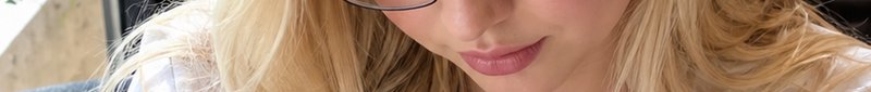 Tight cropped close up of a blonde woman in glasses, soft pink lips, looking downwards