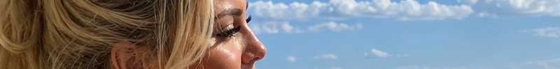 Side profile close up of a blonde woman with closed eyes against a bright blue cloudy sky