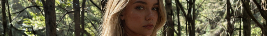 Close up horizontal portrait of a blonde woman with a serious expression, set against a sunlit forest background