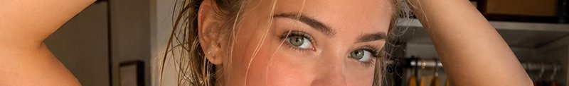 Close up portrait of a woman with bright green eyes holding her hair up in warm indoor light