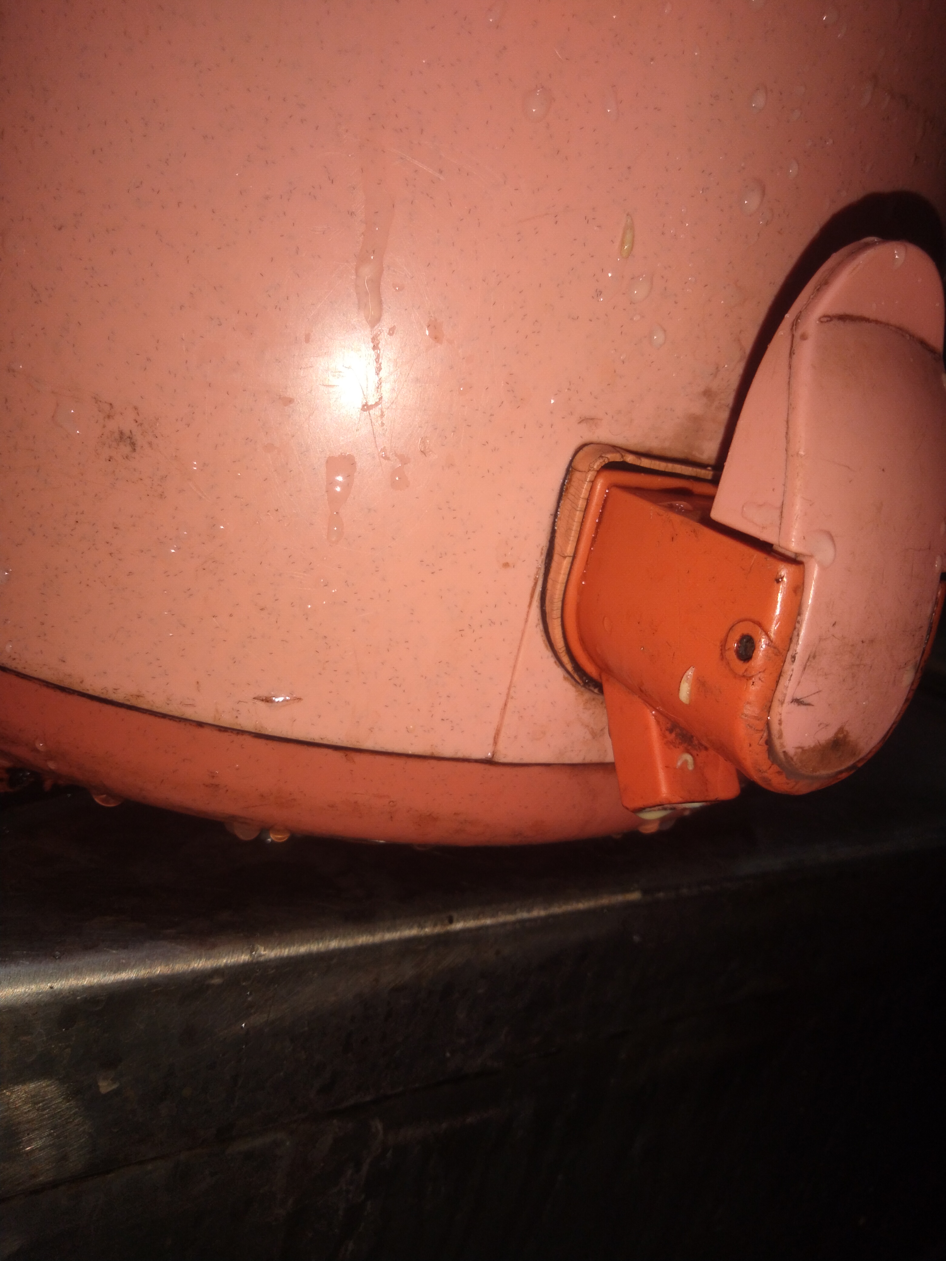 Close up of a wet, stained pink rice cooker hinge and latch resting on a dark kitchen stovetop