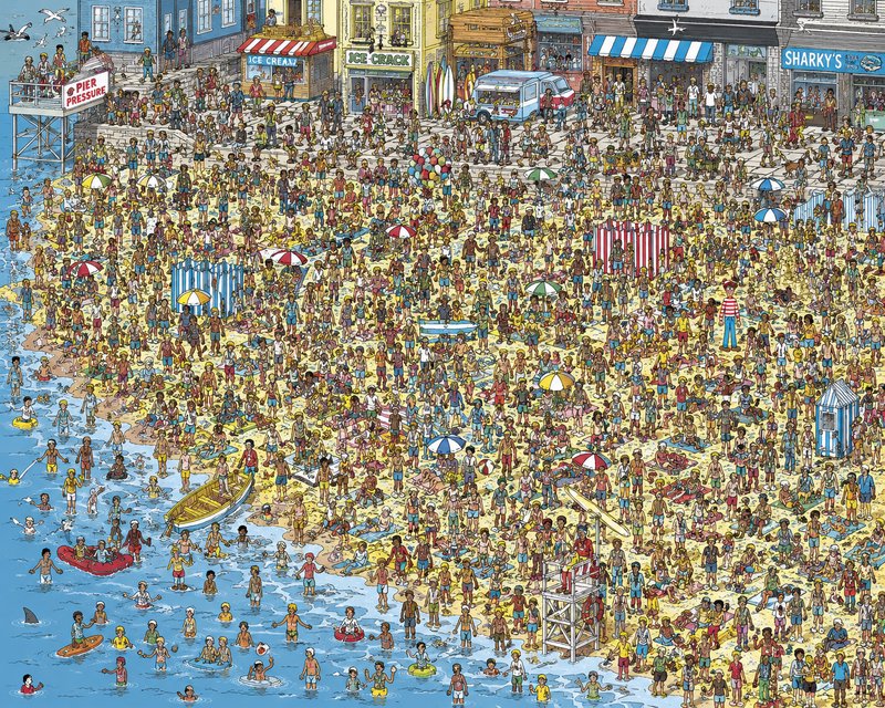 Very crowded beach scene in a seaside town with swimmers, umbrellas, and colorful storefronts.