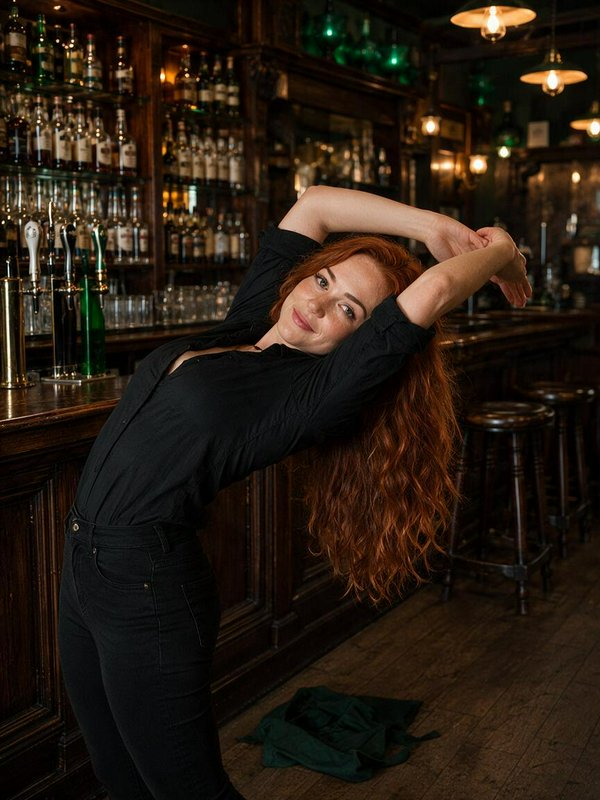 Smiling woman with long wavy red hair stretches playfully next to a dark wood traditional pub bar...