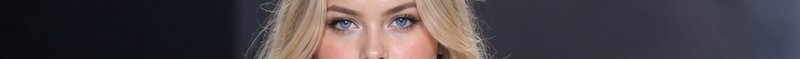 Extreme close-up of a woman's bright blue eyes framed by wavy blonde hair against a dark gradient...