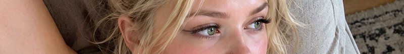 Close-up of a blonde woman with bright green eyes reclining on a fabric couch