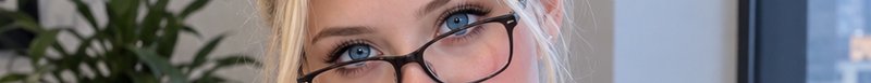 Extreme close-up of bright blue eyes on a blonde woman wearing dark framed eyeglasses indoors
