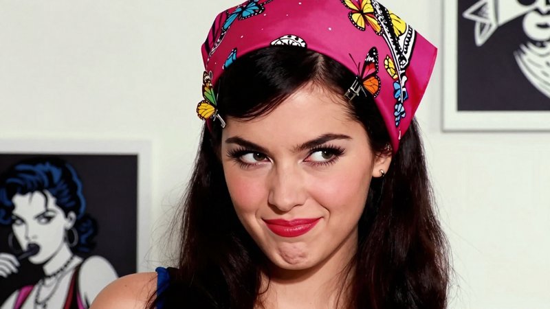 Young woman with pink butterfly print headscarf smirks and glances sideways off camera