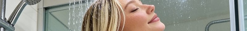Close up of a relaxed streaked blonde woman with closed eyes enjoying running water in a modern s...