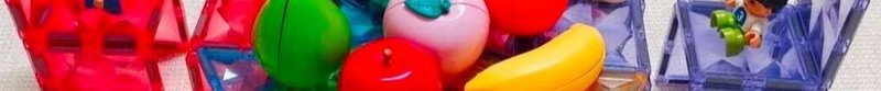 Close up of colorful magnetic building tiles, plastic play fruit, and a small toy figurine on a s...