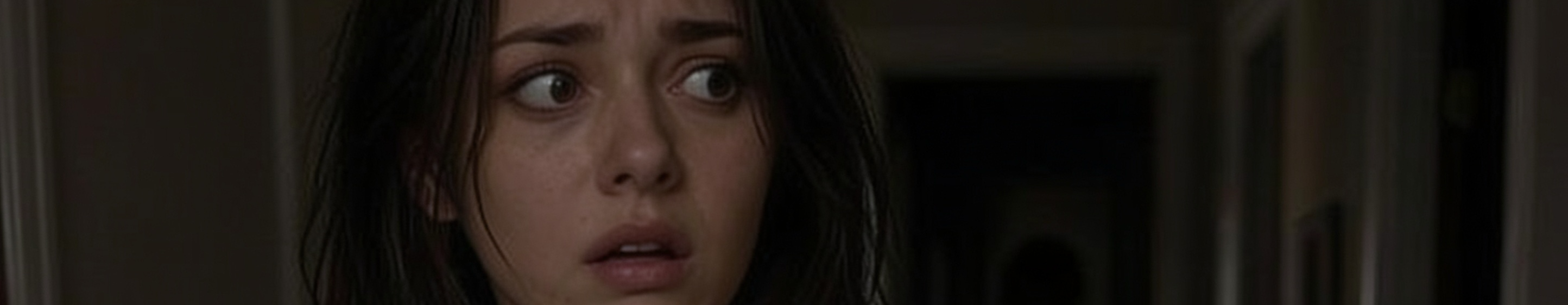 Terrified young woman with dark hair stares anxiously in a dim residential hallway