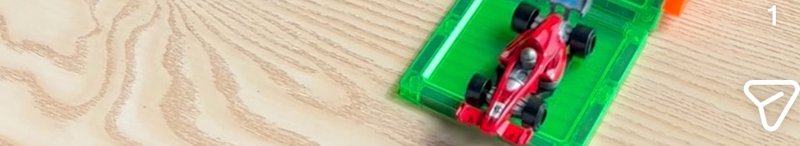 Red toy formula race car sits on a green plastic track segment atop a light wooden table
