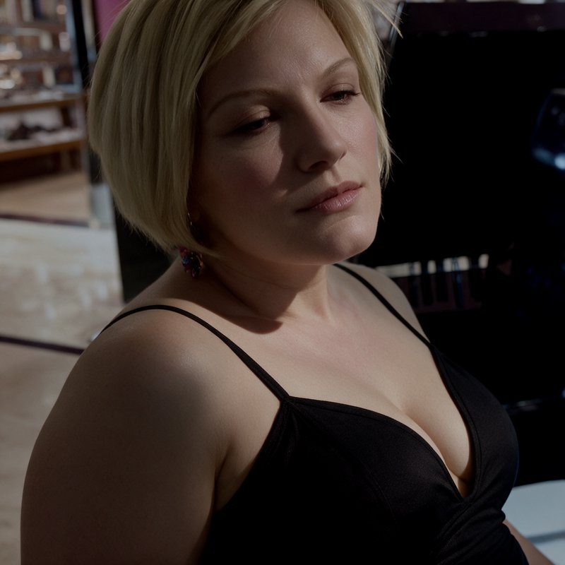 Pensive woman with short blonde bob wears a black spaghetti strap dress, lit by soft dramatic sid...