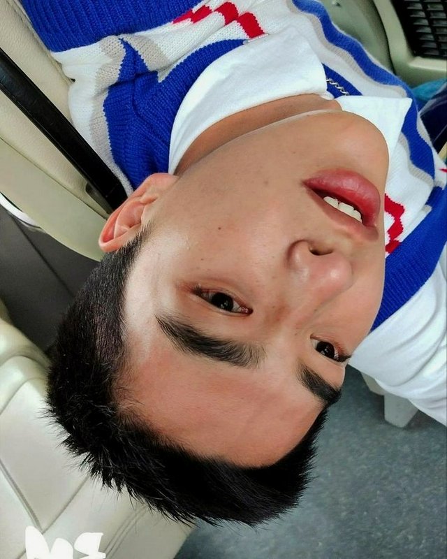 Young man with short black hair in a blue, white, and red striped sweater inside a car.