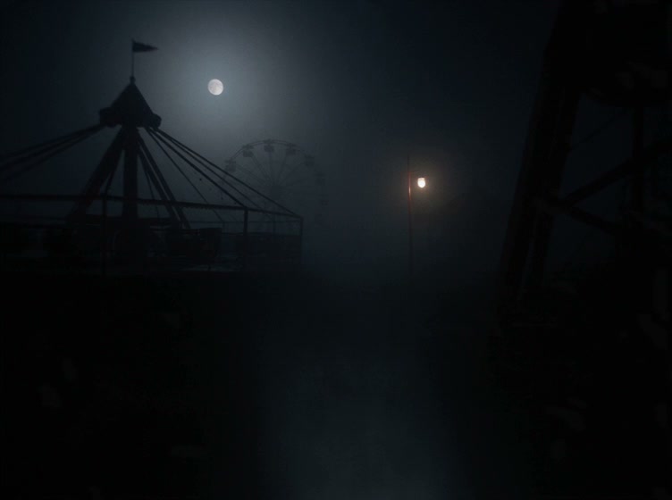 Silhouetted abandoned amusement park rides stand in thick fog under a glowing full moon at night