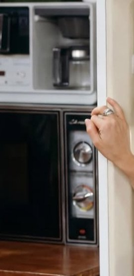 Person opening a cabinet beside a built-in microwave and wall oven in a modern kitchen.