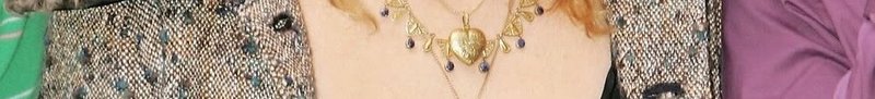 Close-up of a person wearing a gold heart pendant necklace with purple beads over a patterned, metallic jacket.