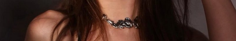 Close-up of a silver chain necklace on a person with dark hair under warm lighting.