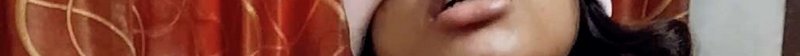 Close-up of a person’s lower face with warm orange-red fabric in the background.