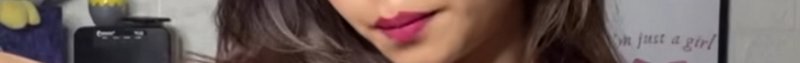 Close-up portrait of a woman with pink lipstick and wavy brown hair in soft studio lighting.