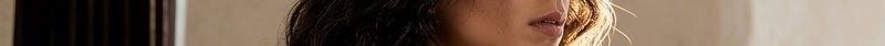 Close-up portrait of a woman with wavy hair bathed in warm lighting.