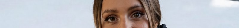 Close-up of a woman's eyes and forehead against a pale neutral background.