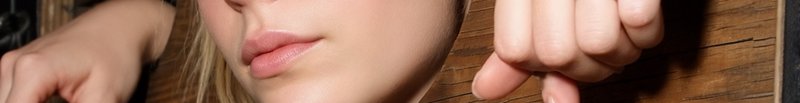 Close-up of a woman's lower face with pink lips and a hand resting on a wooden surface.