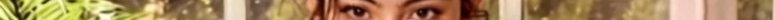 Close-up of a person’s eyes peering through yellow-green foliage in sunlight.