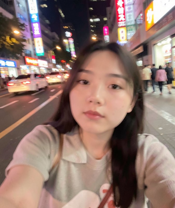 Young woman taking a night selfie on a neon-lit city street with cars and colorful signs.
