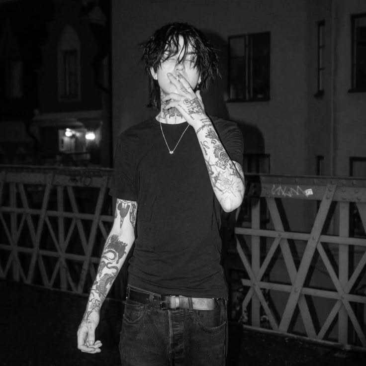 Black-and-white photo of a tattooed man in a black t-shirt covering part of his face on a night u...