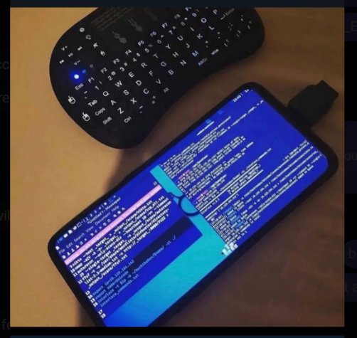 Smartphone with a blue terminal screen showing code beside a wireless keyboard on a desk.