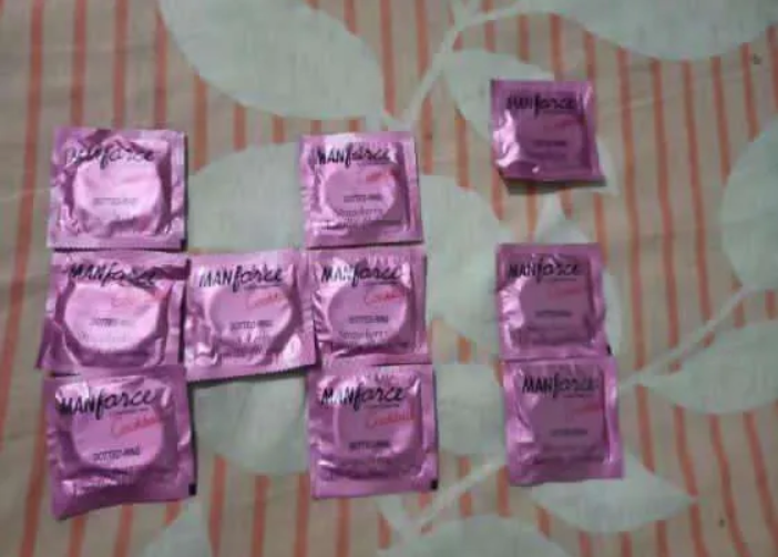 Ten shiny pink Manforce condom foil packets arranged on a striped leaf-print bedsheet.