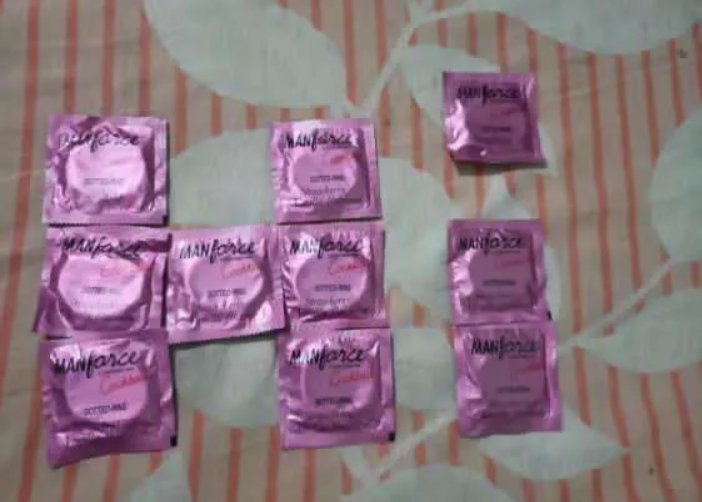 Ten shiny pink Manforce condom foil packets arranged on a striped leaf-print bedsheet.