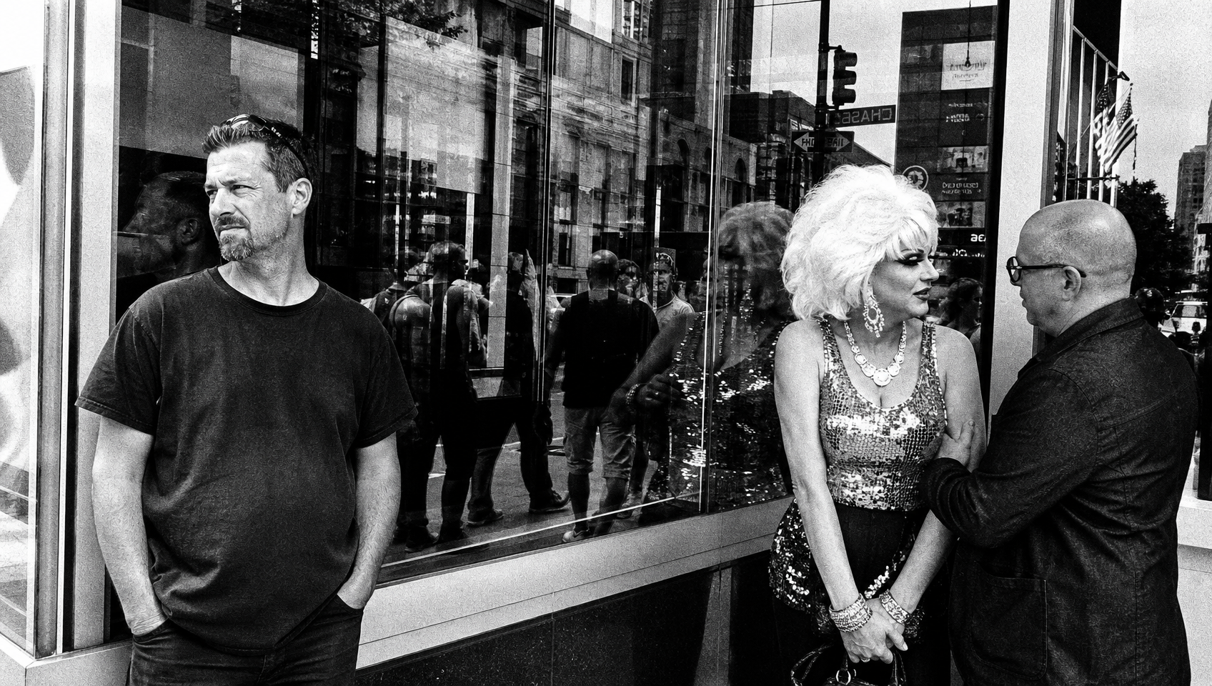 Black and white candid street shot of three people standing outside a downtown storefront with glass window reflections