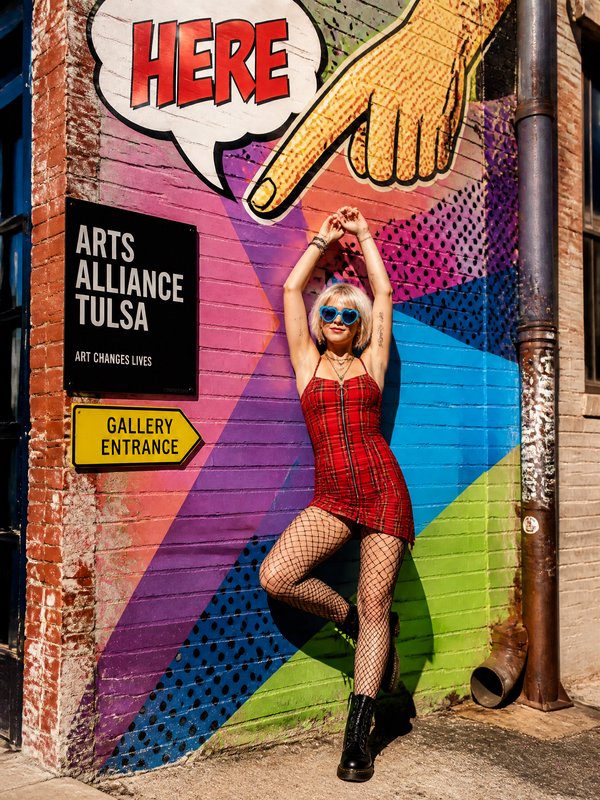 Trendy woman in red plaid dress poses against colorful pop art mural outside Arts Alliance Tulsa gallery