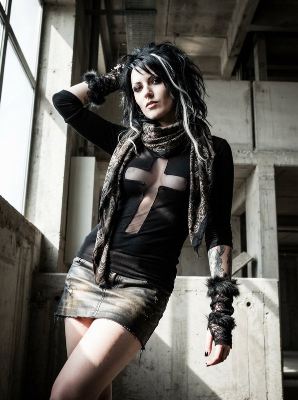 Tattooed goth fashion model posing in sunlit unfinished concrete industrial building