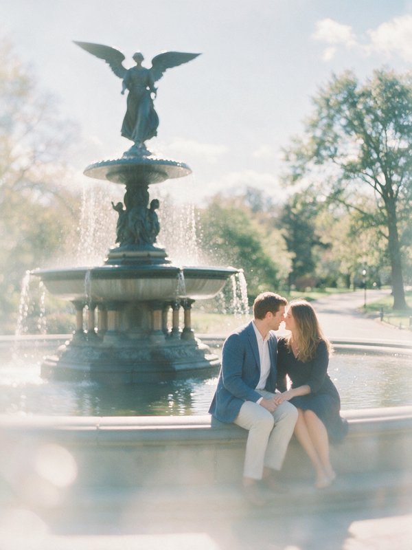 Engaged couple sitting face to face on the edge of Bethesda Fountain in sunlit Central Park