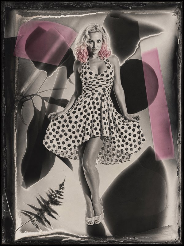Pinup model with pink-tipped blonde hair in a polka dot dress poses against a vintage abstract photo background