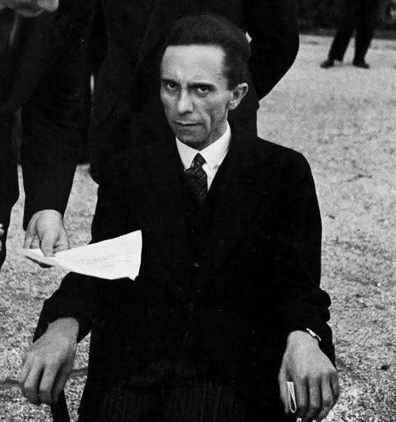 Black-and-white photo of a man in a suit seated outdoors, holding papers.