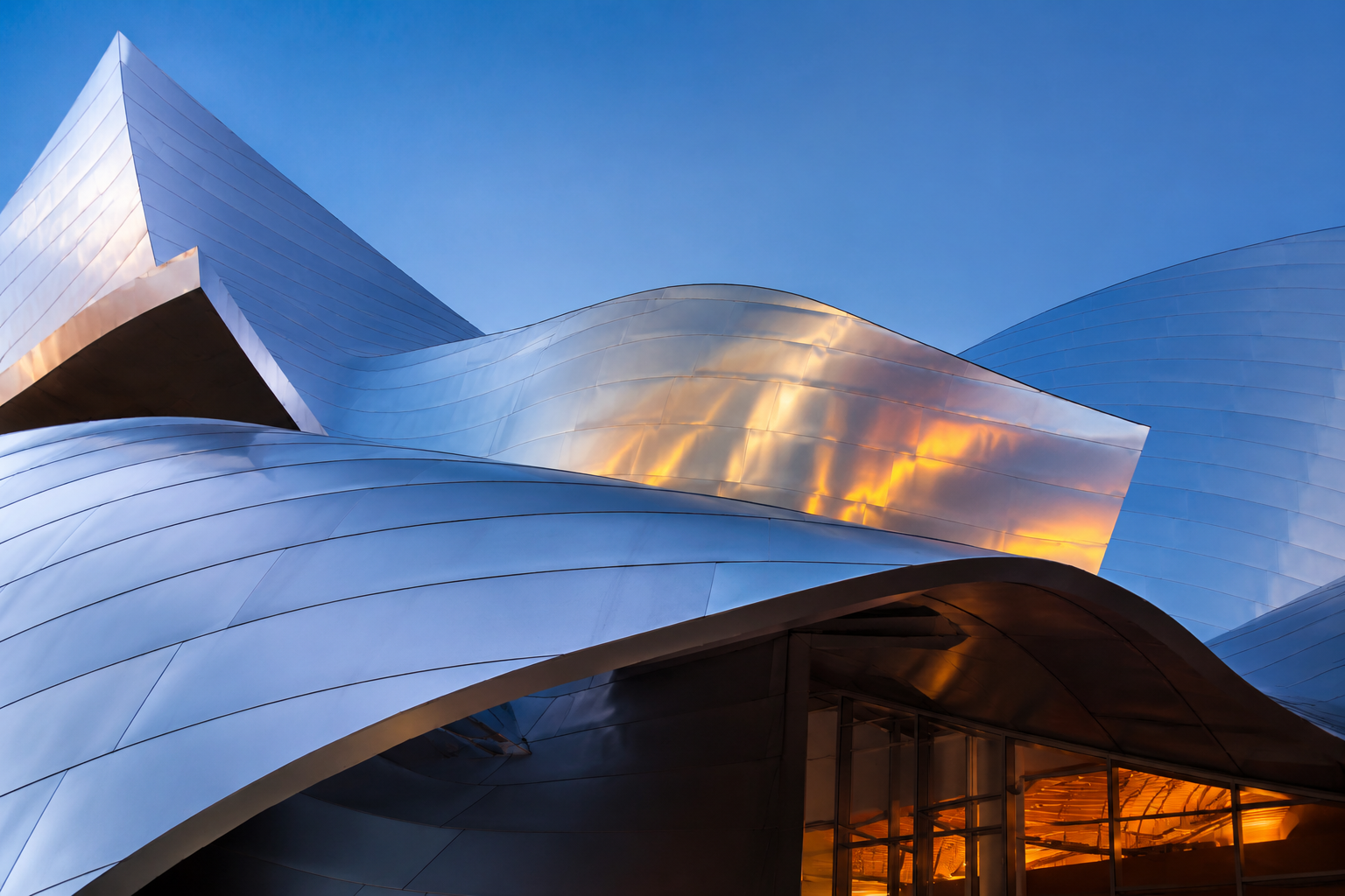 Shiny curving stainless steel architecture against a blue evening sky with warm interior glow
