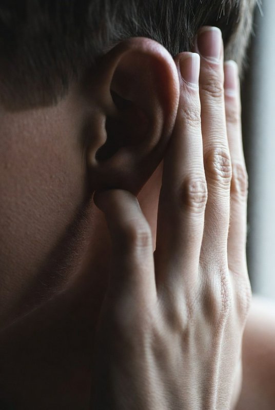 Close-up of a person cupping their ear with their hand, listening intently.