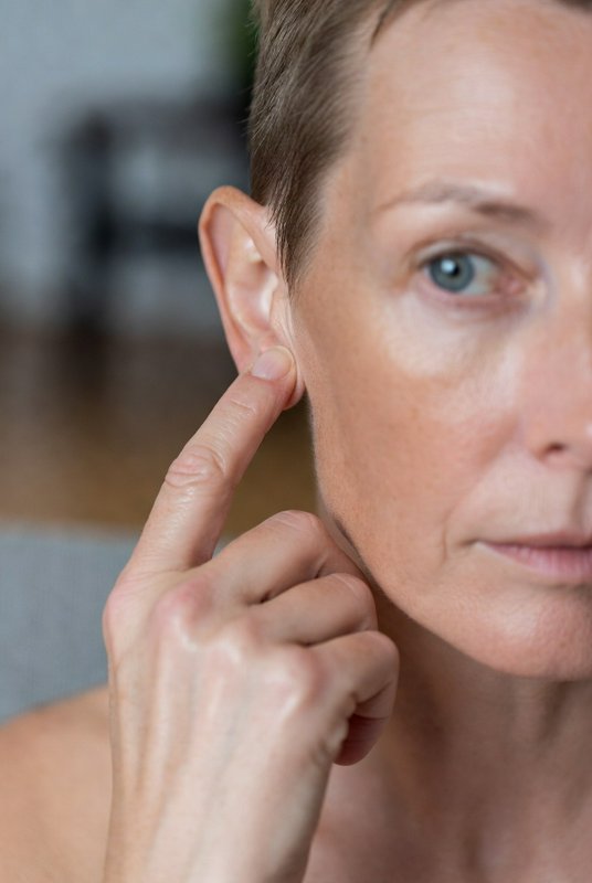 Close-up of a person touching their ear, focusing on the earlobe and side of the face.