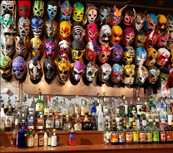 Colorful lucha libre masks displayed on a wall above a well-stocked bar
