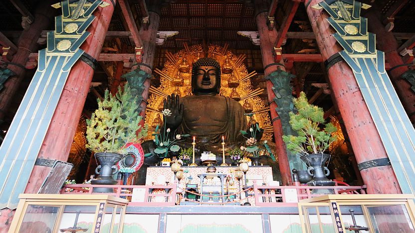 Large seated Buddha statue inside an ornate temple altar with candles and plants.