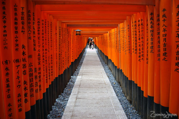 Orange torii gate path at Fushimi Inari Shrine with kanji inscriptions and a sunlit walkway