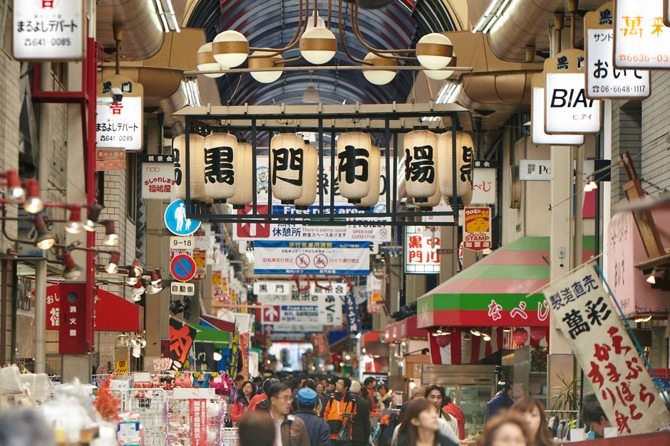 Busy Japanese shopping street with hanging lanterns and colorful signs.