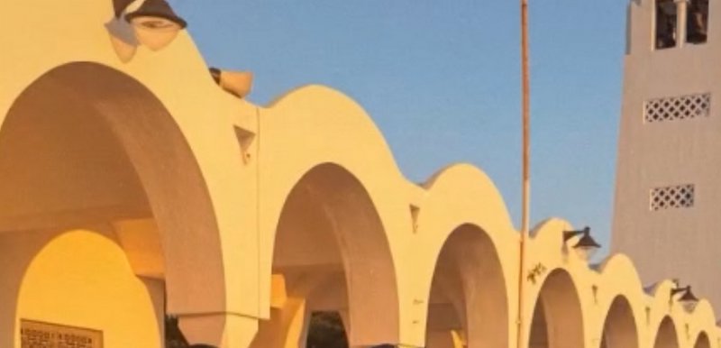 Warm golden hour light illuminates curved white arched Mediterranean architecture beside a stucco...