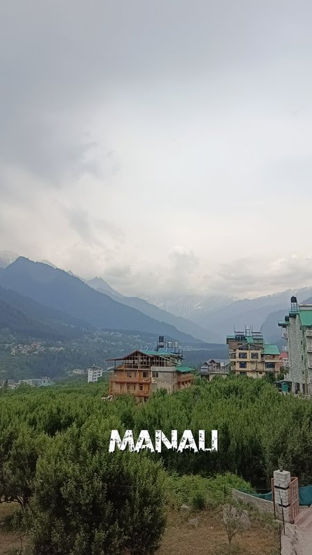 Hillside Manali town with mountains, cloudy sky, and buildings under construction amid green trees.