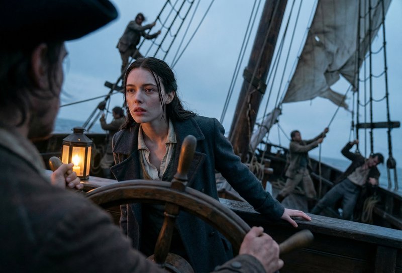 Woman on a vintage sailing ship at dusk, lantern in hand, steering with crew working the rigging.