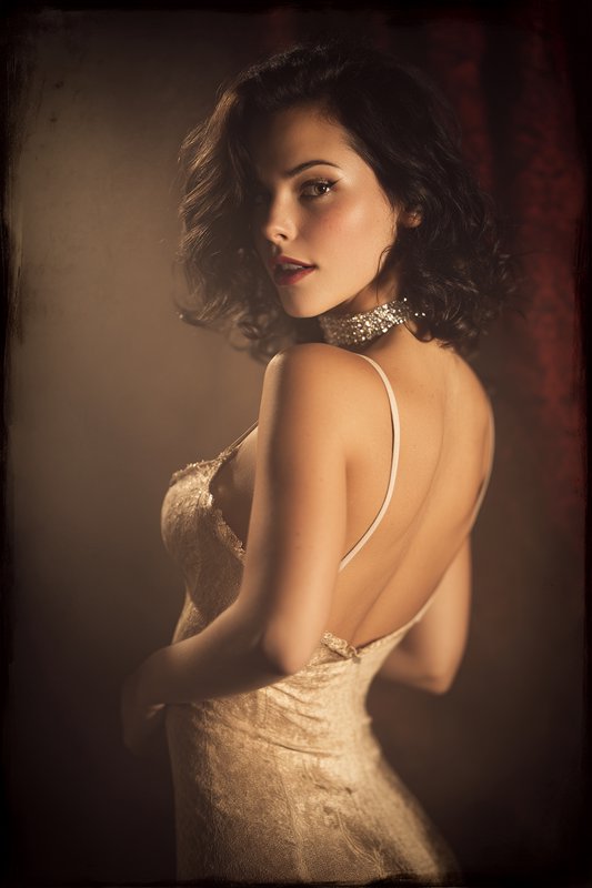 Old Hollywood glamour portrait of a woman with wavy dark hair looking over her shoulder, wearing ...