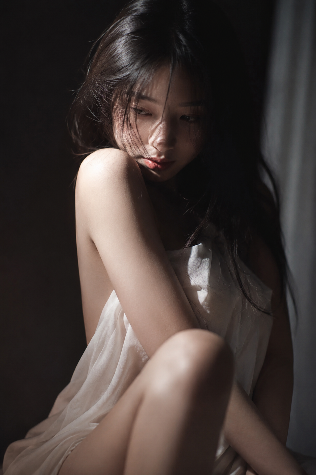 [Low-key intimate portrait of young East Asian woman in sheer white dress, lit by soft dramatic side light against dark ba...